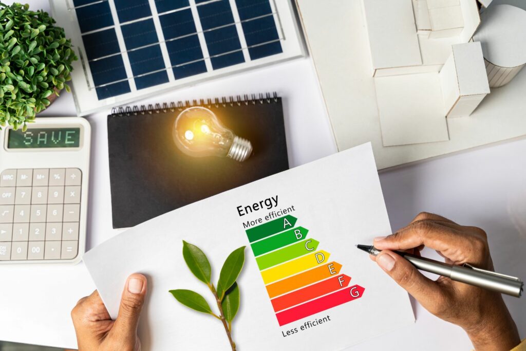 Immagine che mostra un grafico di efficienza energetica con scale colorate da A a G, una persona che annota su un foglio, una lampadina accesa, un calcolatore e pannelli solari, evidenziando l'importanza del risparmio energetico.